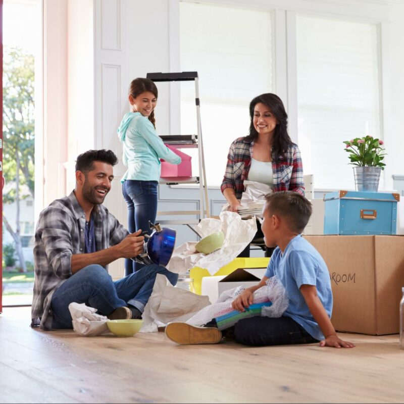 Happy family unpacking boxes in their new home, with parents and children smiling and enjoying the process of moving in.
