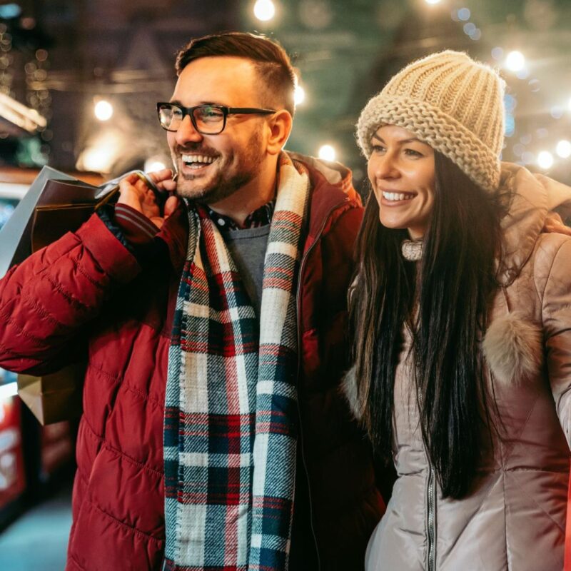 Smiling couple carrying shopping bags at a festive outdoor market during the holiday season