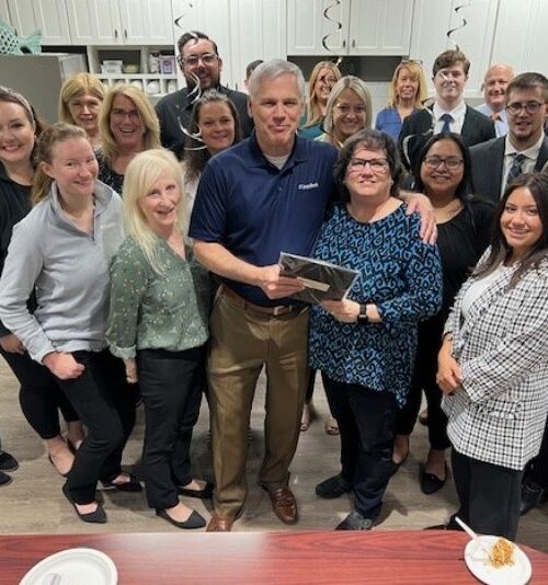 Group photo of a team gathered in an office setting, smiling and celebrating together.