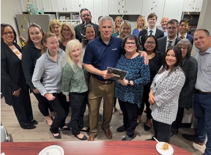 Group photo of a team gathered in an office setting, smiling and celebrating together.